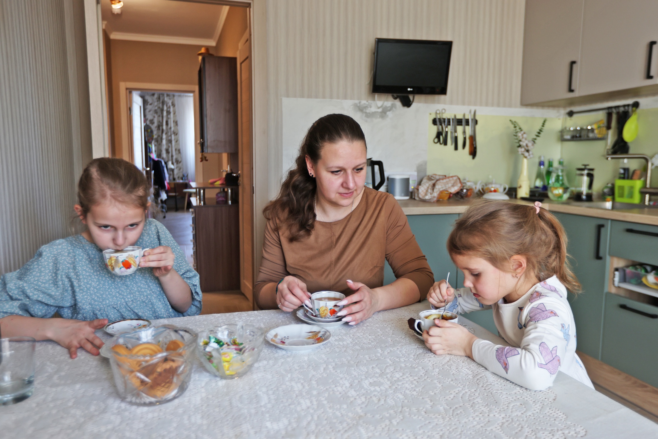 Мама с двумя дочерьми пьют чай в новой квартире